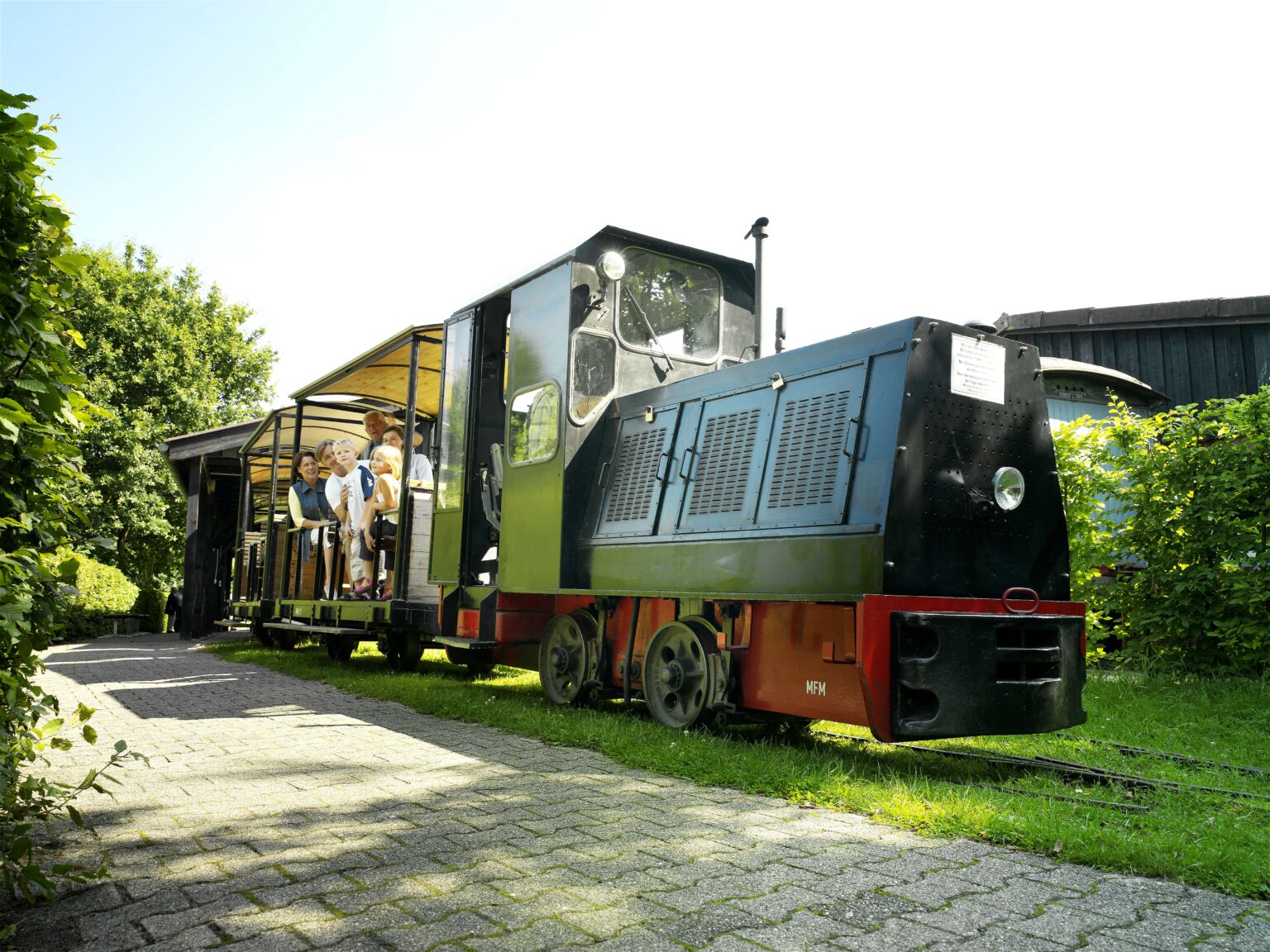 Im Emsland Moormuseum fährt eine grüne Museumslok mit Fahrgästen auf schmaler Strecke durch viel Grün.