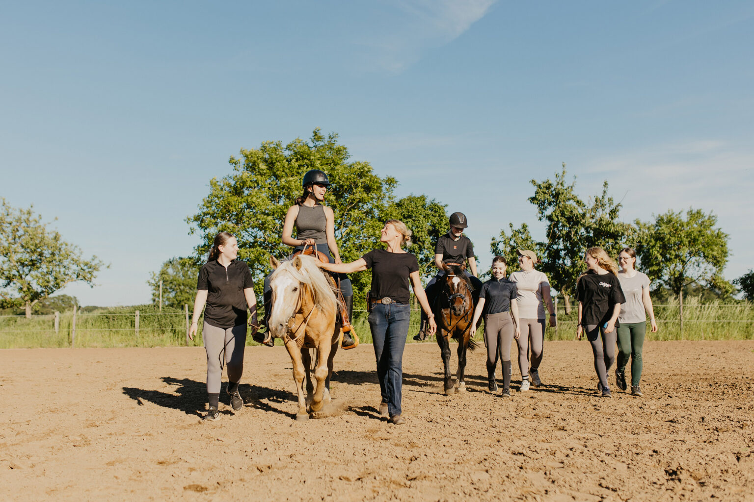 Bei Gut Landegge führt eine Reiterlebnis-Gruppe mit Ponys und Betreuerinnen über den sonnigen Reitplatz.