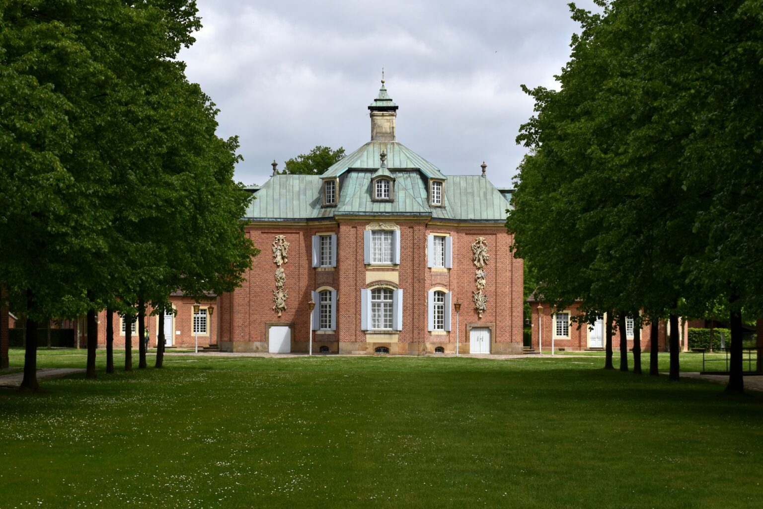 Das barocke Schloss Clemenswerth in Sögel steht zwischen grünen Bäumen vor einer weitläufigen Rasenfläche.