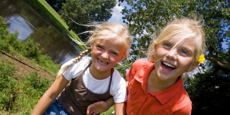 Familienhotel Gut Landegge im Emsland: zwei Mädchen lachen am Uferrand in die Kamera