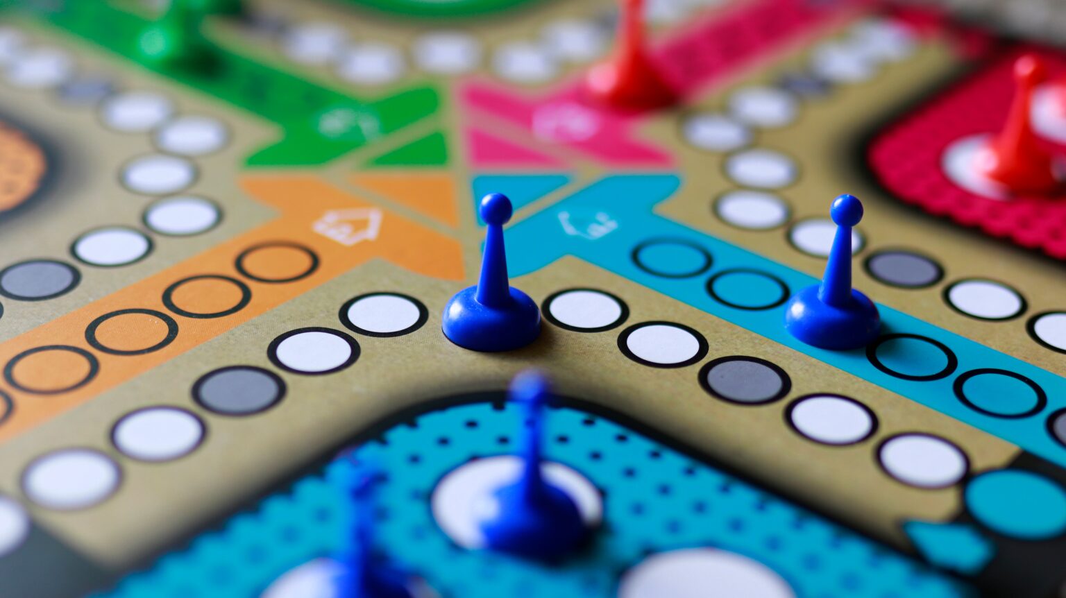 Bunte Spielfiguren stehen auf einem farbigen Spielbrett mit Feldern und Rundwegen für Gesellschaftsspiele.