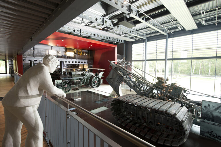 Im Emsland-Moormuseum stehen eine weiße Mammutfigur und historische Landmaschinen in einer hellen Ausstellungshalle.